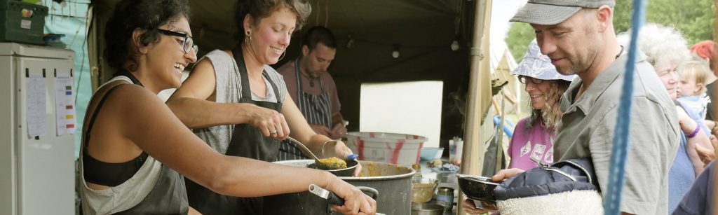 smiling caterers serving healthy tasty food to people from a nice canvas marquee at radical bakers